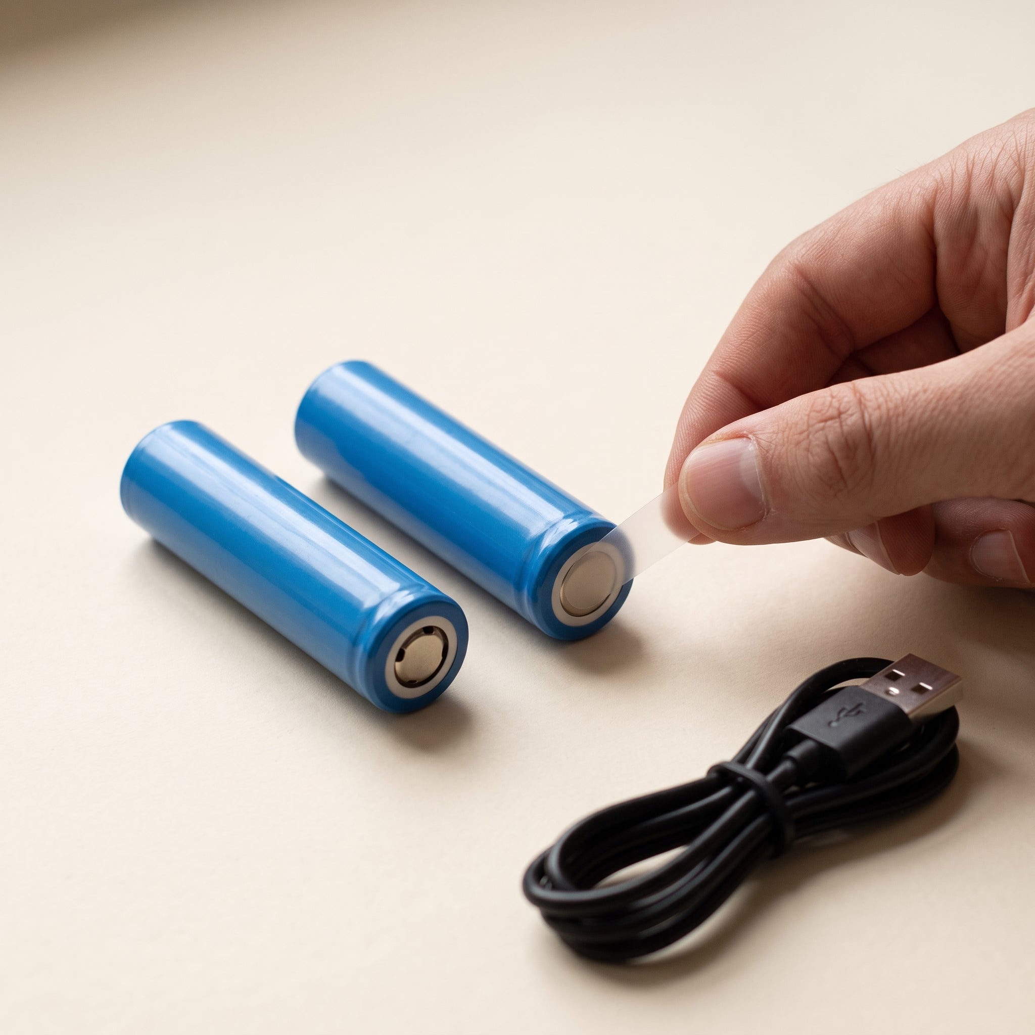 Deux batteries rechargeables et le câble USB fourni, posés sur un plan crème